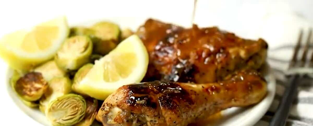 White plate with balsamic lemon chicken, Brussels sprouts, and lemon wedges.