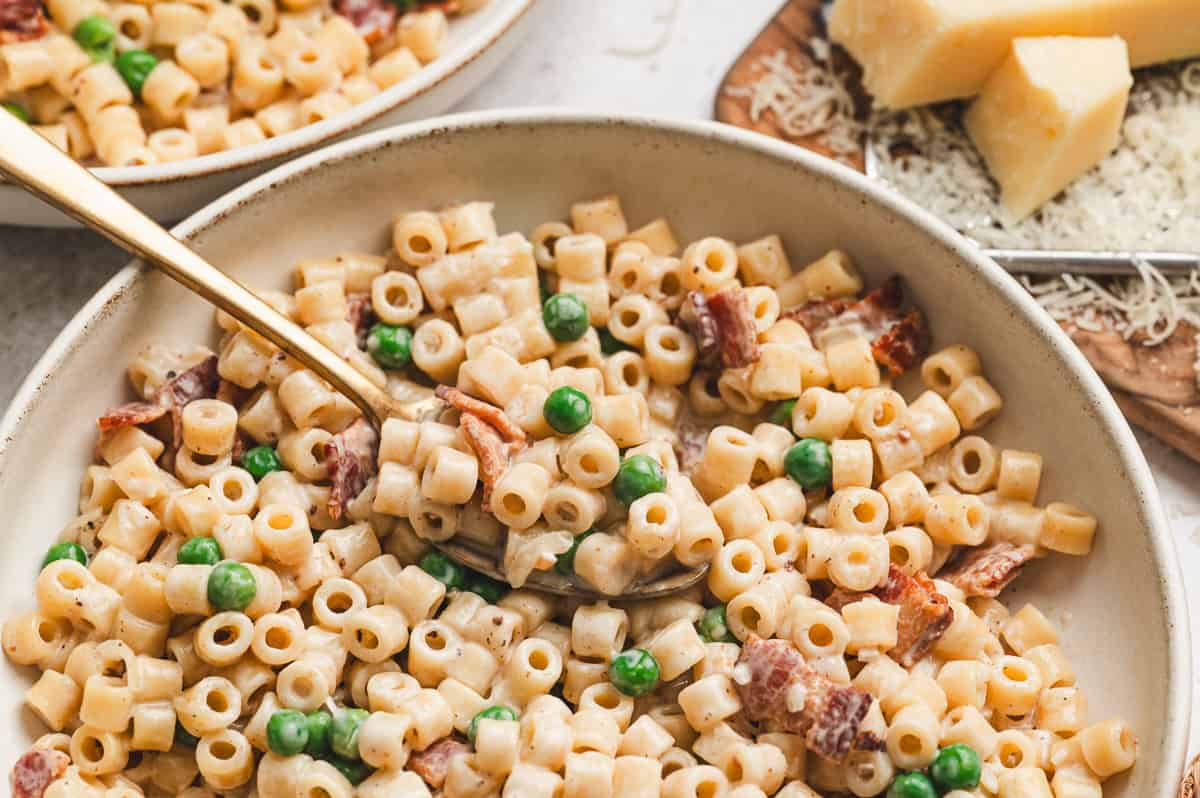 Creamy bacon pea pasta served in a bowl with crispy bacon, sweet peas, and a rich Parmesan sauce, with a fork lifting a bite.