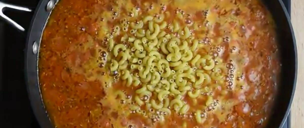 Adding sauce and macaroni to the pan with the onions and pepperoni.