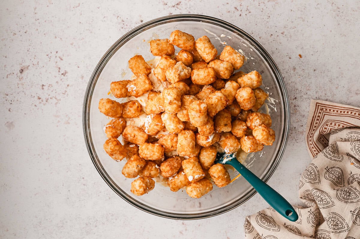 Tater tots in a glass bowl covered with the cheese mixture.