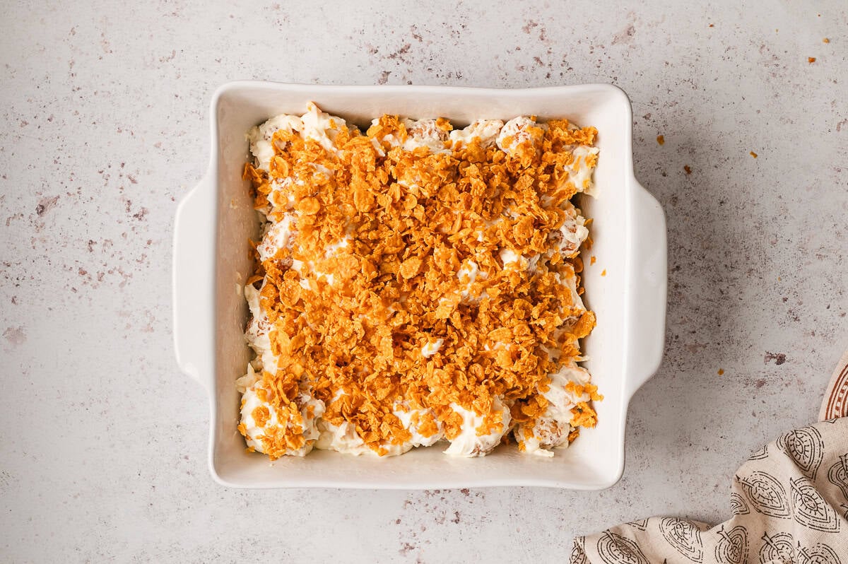 Tater tots in a white casserole dish coated with the cheese mixture and topped with the corn flake topping.