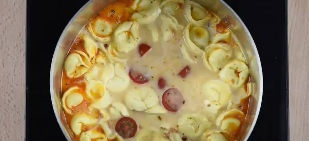 Adding cherry tomatoes to the pot of tortellini.