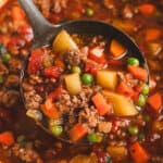 Chuck Wagon Stew with ground beef, potatoes, carrots, peas, and tomatoes in a rich savory broth served in a ladle.