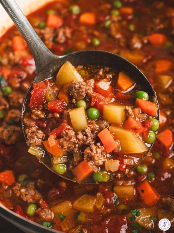Chuck Wagon Stew with ground beef, potatoes, carrots, peas, and tomatoes in a rich savory broth served in a ladle.