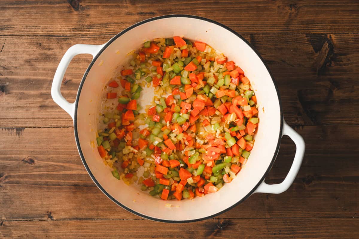 Diced onions, carrots, and celery sautรฉing in olive oil in a Dutch oven to build flavor for chuck wagon stew.