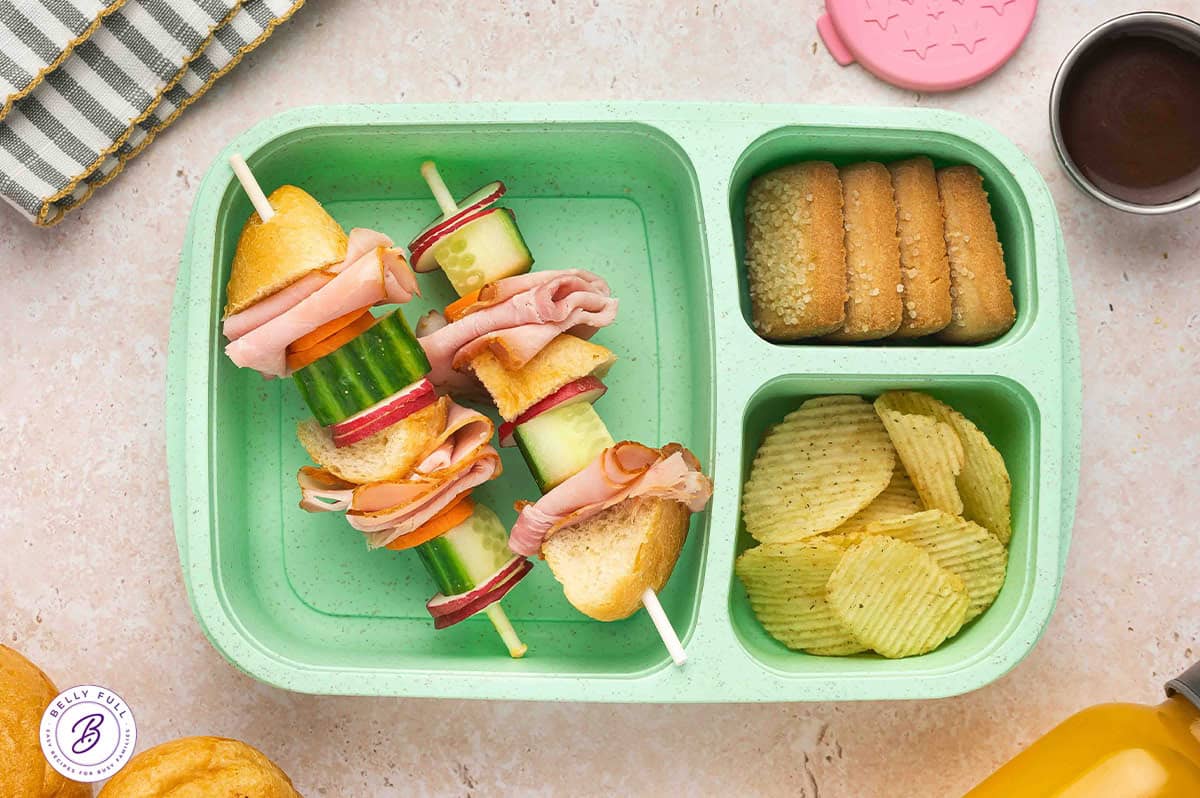 Banh Mi sandwich on a stick made with pieces of french baguette, ham, carrot, cucumber, radish, in a lunch box