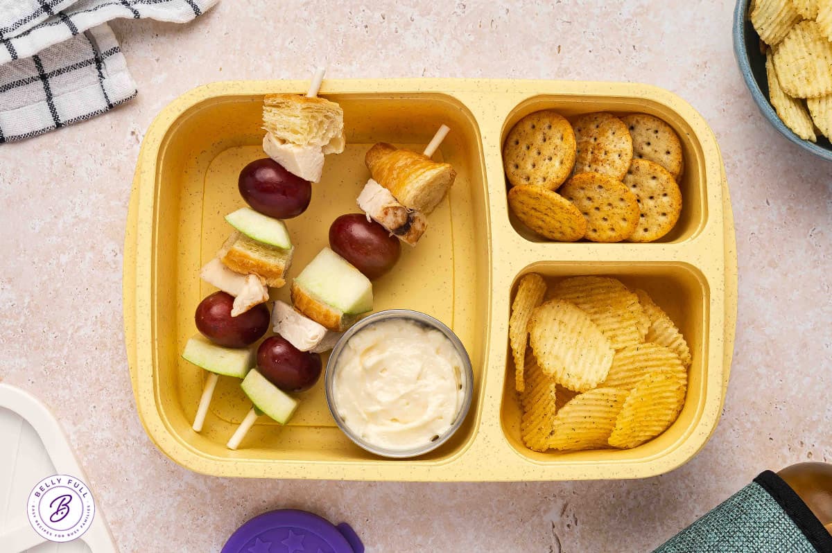 Chicken Salad on a stick with croissant pieces, chicken, red grapes, and green apple in a lunch box
