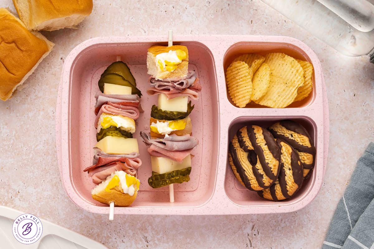 Cubano sandwich on a stick with Hawaiian rolls, sliced ham, sliced cooked pork, Swiss cheese, dill pickle hamburger chips in a lunchbox