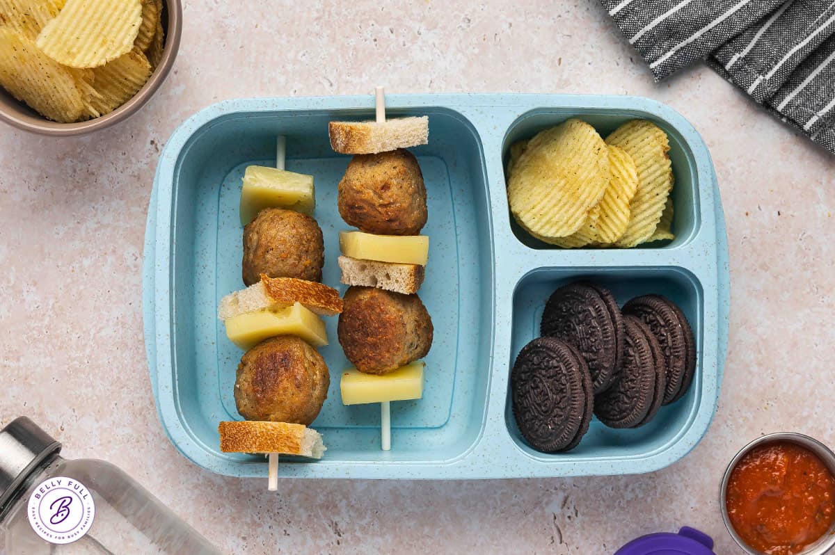 Meatball Sub sandwich on a stick with pieces of sourdough bread, cooked Italian meatballs, and provolone in a lunch box