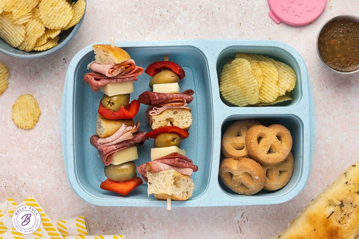 Muffuletta sandwich on a stick with focaccia pieces, ham, salami, mozzarella, olive, red bell pepper, in a lunch box