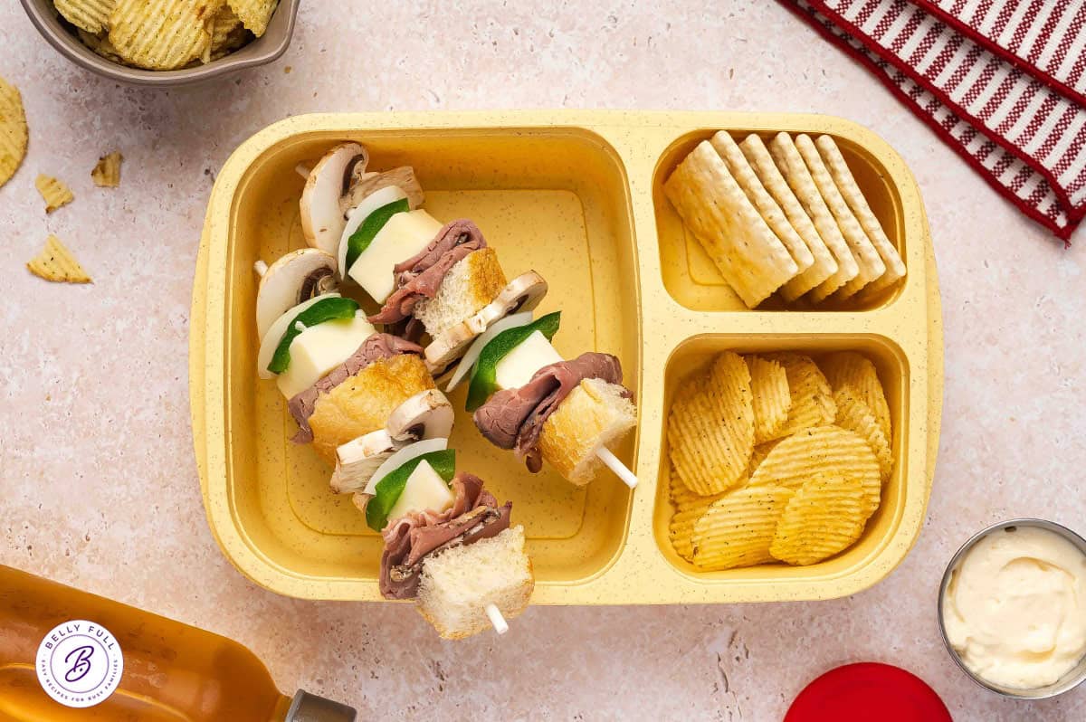 Philly Cheesesteak sandwich on a stick with hoagie roll pieces, roast beef, provolone, green pepper, onion, mushroom in a lunchbox