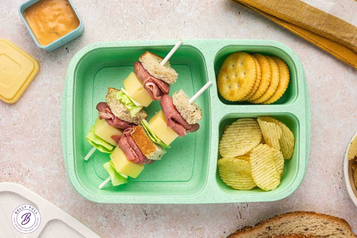 Reuben sandwich on a stick with rye bread pieces, corned beef, swiss cheese, and cabbage in a lunch box