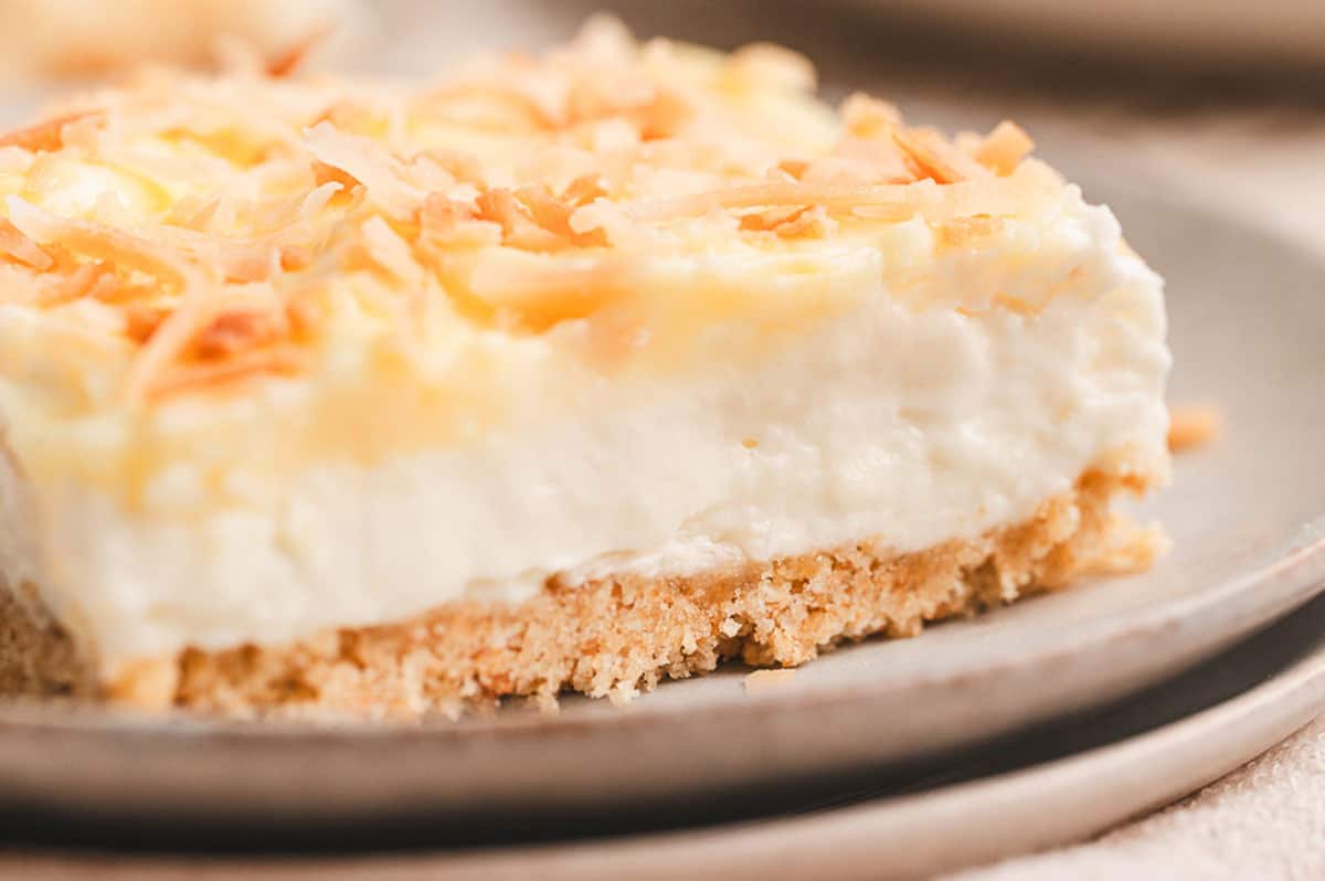 This Coconut Cream Lush is smooth, rich, light, and there’s no cooking involved. It’s so easy and perfect for summer gatherings! Side view of a slice of coconut cream lush on a plate