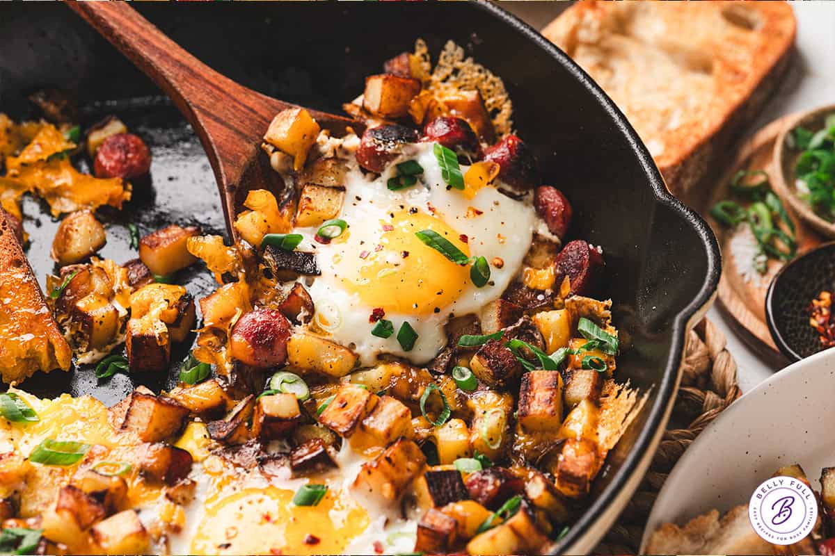 Smoked sausage, diced potatoes, egg, and cheese make this Skillet Breakfast Hash an easy, savory, and hearty breakfast. A wooden spoon serving skillet breakfast hash