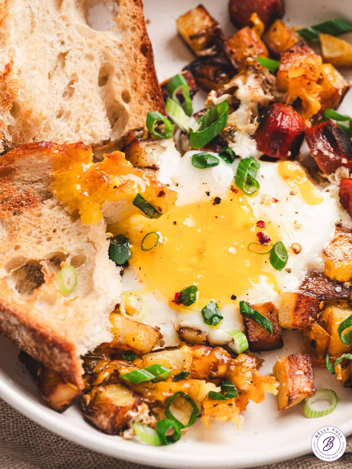 Smoked sausage, diced potatoes, egg, and cheese make this Skillet Breakfast Hash an easy, savory, and hearty breakfast. Close up of skillet breakfast hash with crusty bread