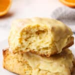 Close up of two orange creamsicle scones on a plate, one with a bite missing to show the inside
