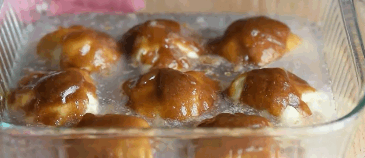 Peach dumplings in a baking dish with soda poured around them. 