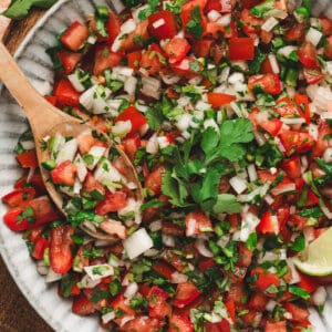 Bowl of fresh pico de gallo with tomatoes, onion, jalapeño, and cilantro, served with a wooden spoon