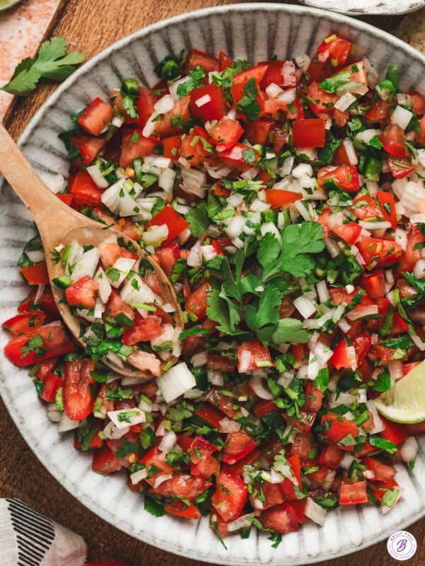 Bowl of fresh pico de gallo with tomatoes, onion, jalapeño, and cilantro, served with a wooden spoon