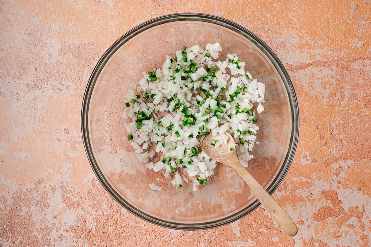 Finely diced white onion and jalapeño mixed in a glass bowl for pico de gallo base