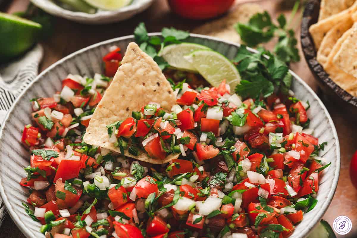 Fresh pico de gallo served with tortilla chips and lime wedges in a bowl