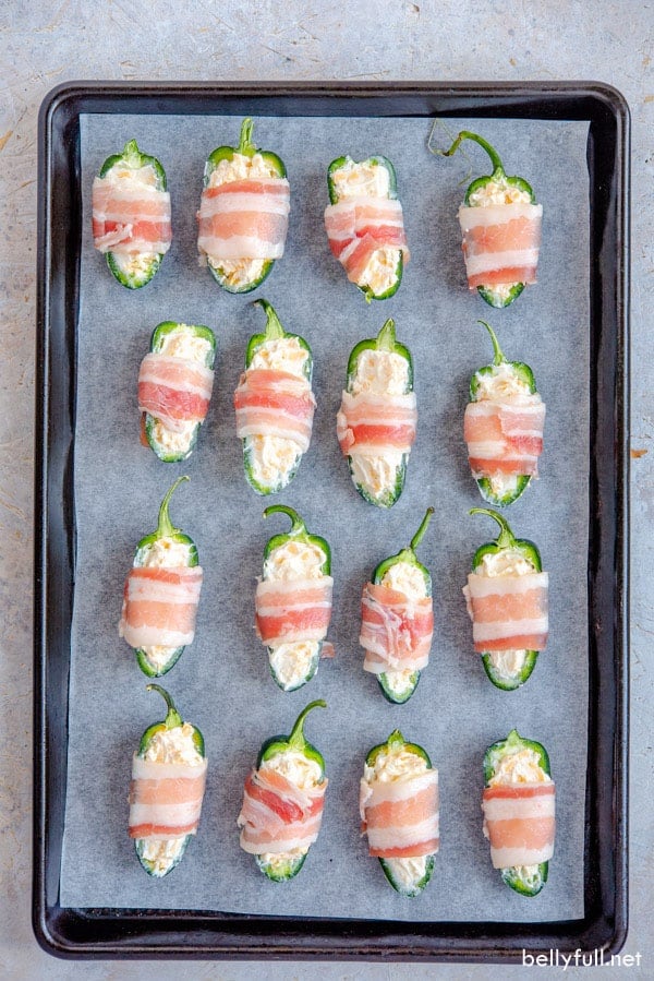 jalapeno peppers stuffed with cream cheese, wrapped in bacon on baking sheet