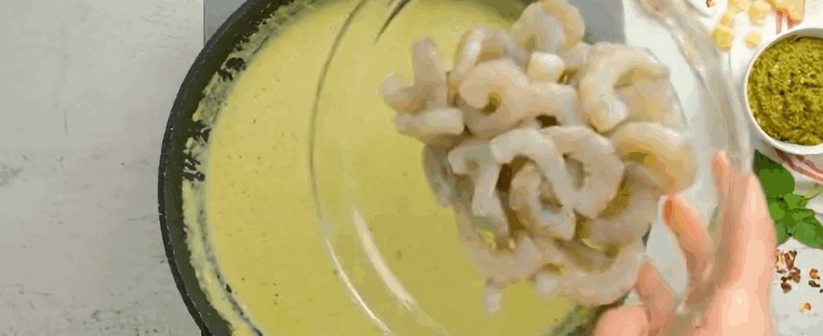 Adding pesto and shrimp to the sauce.