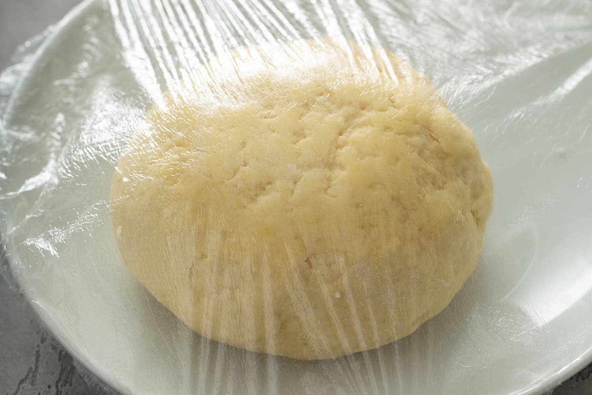 Pierogi dough wrapped in plastic wrap on a white plate.