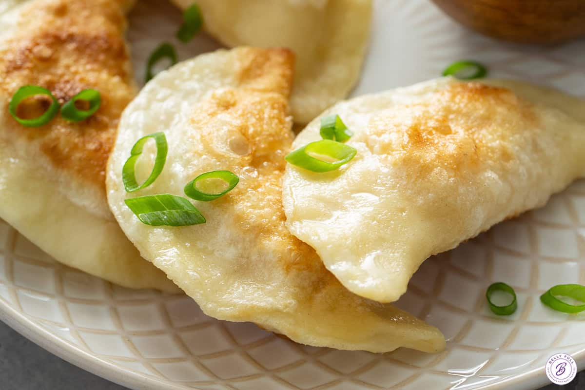 Pan fried pierogi garnished with green onions on a plate.