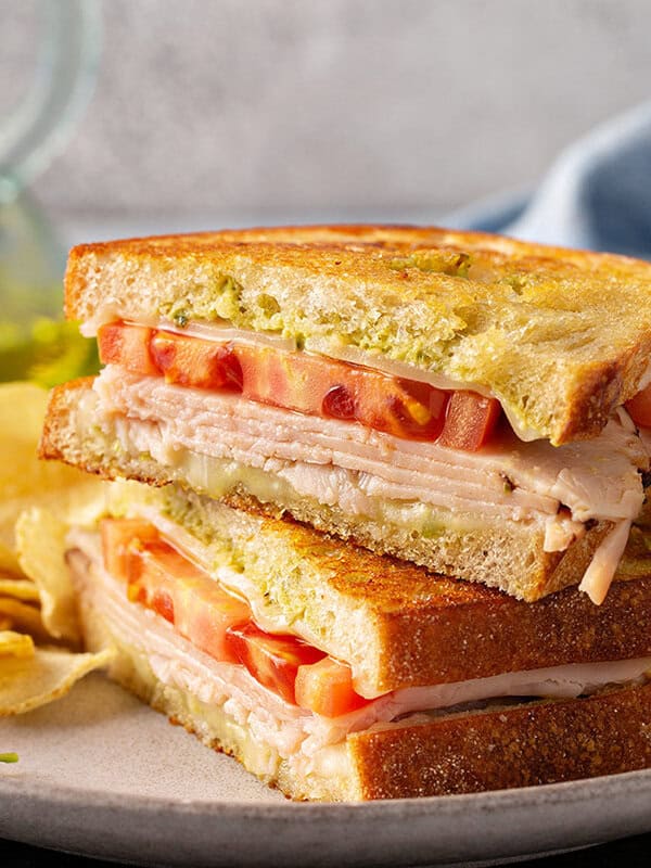 pesto grilled cheese sandwich cut in half and stacked on plate