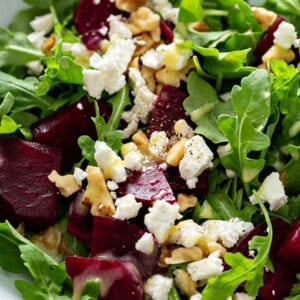 close up picture of baby arugula salad with diced roasted beets, chopped walnuts, and crumbled feta cheese