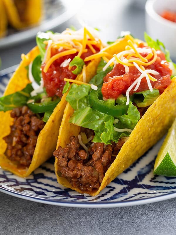2 crispy tacos on ornate plate topped with lettuce and salsa