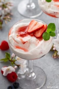 mixed berry fruit fool in parfait glass with sliced strawberries and fresh mint leaves