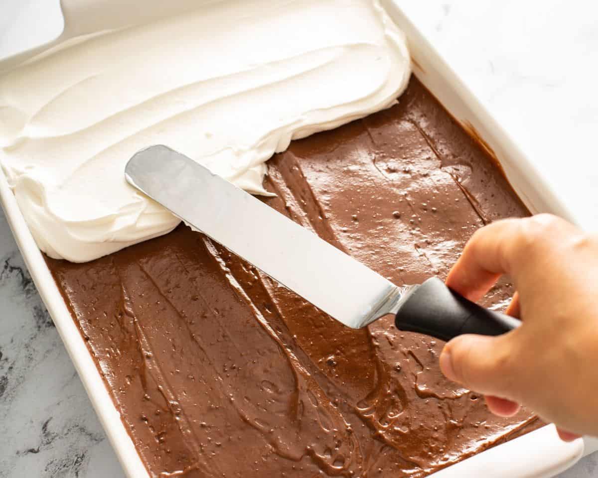 Cool Whip being spread over the pudding layer of the chocolate lasagna.