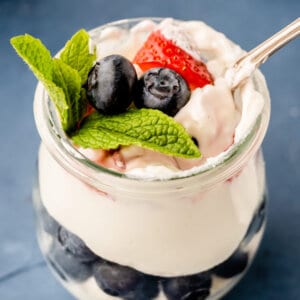 overhead picture of blueberries and strawberries, with mint leaf, in cheesecake mousse with spoon