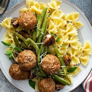 close up overhead picture of cooked turkey meatballs, green beans, mushrooms, and bowtie pasta on white plate