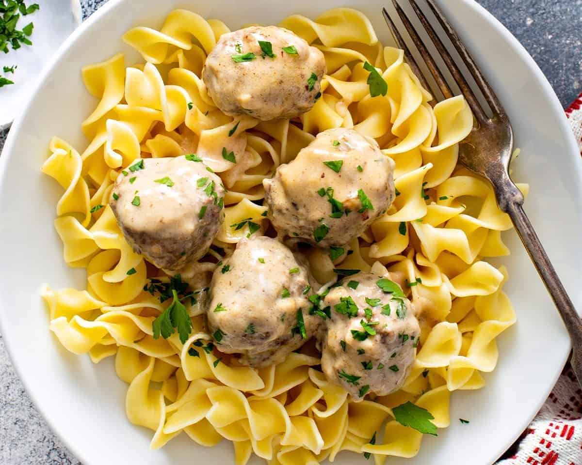 Swedish meatballs over egg noodles on a white plate.