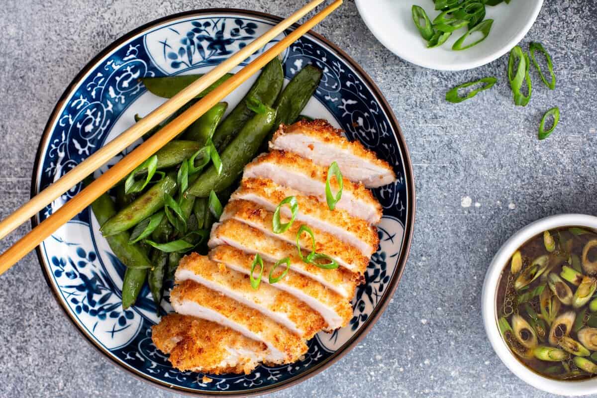 Plate of sliced pork and snap peas with a bowl of dipping sauce on the side.