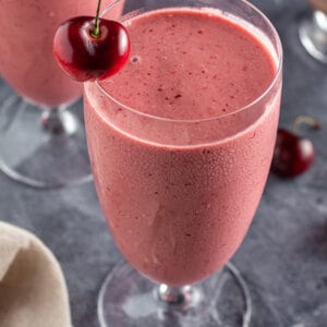 overhead angle of tall glass filled with cherry smoothie with fresh cherry on rim