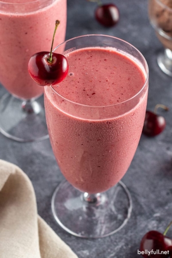 overhead angle of tall glass filled with cherry smoothie with fresh cherry on rim