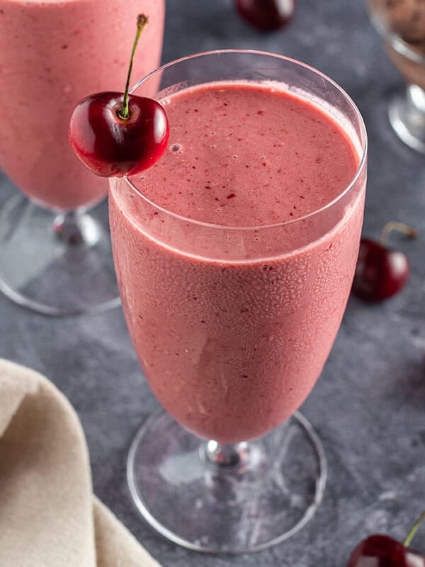 overhead angle of tall glass filled with cherry smoothie with fresh cherry on rim