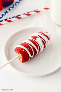 half a frozen banana coated in red chocolate drizzled with white chocolate on a white plate