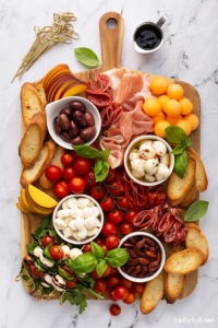 overhead of rectangular meat and cheese board with mozzarella balls, cured meats, fresh peaches, and cherry tomatoes