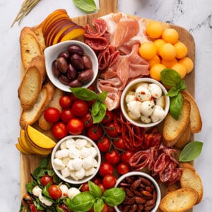 overhead of rectangular meat and cheese board with mozzarella balls, cured meats, fresh peaches, and cherry tomatoes