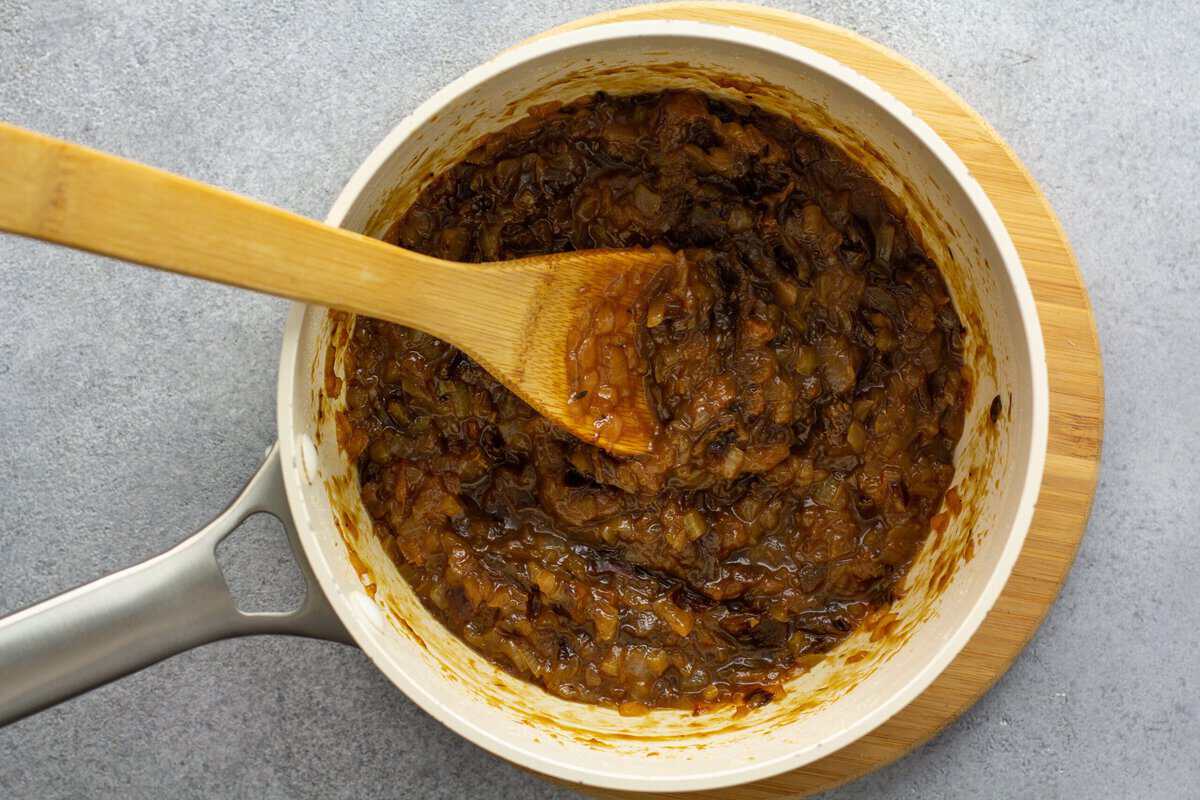Cooking the ingredients to make onion jam in a pot with a wooden spoon.