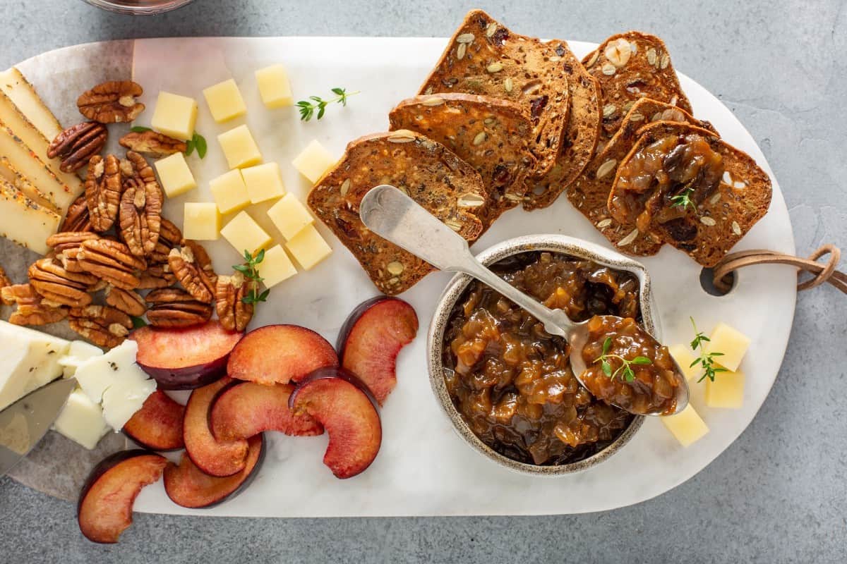 Onion jam on a serving platter with walnuts, cheese, crackers, and plums.