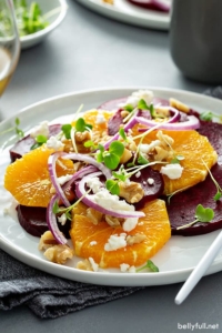 orange beet salad with red onion, feta cheese, and walnuts on white plate