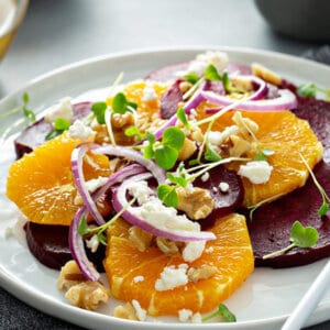 orange beet salad with red onion, feta cheese, and walnuts on white plate