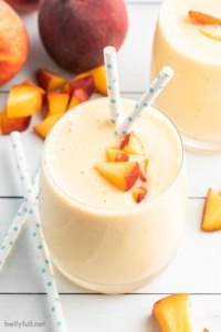 peach smoothie with diced fresh peaches on top and polka dot blue straws