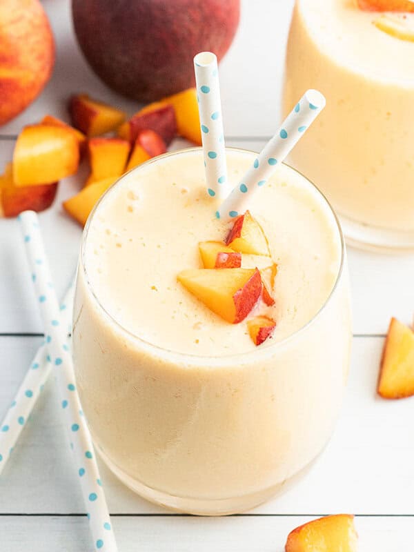peach smoothie with diced fresh peaches on top and polka dot blue straws